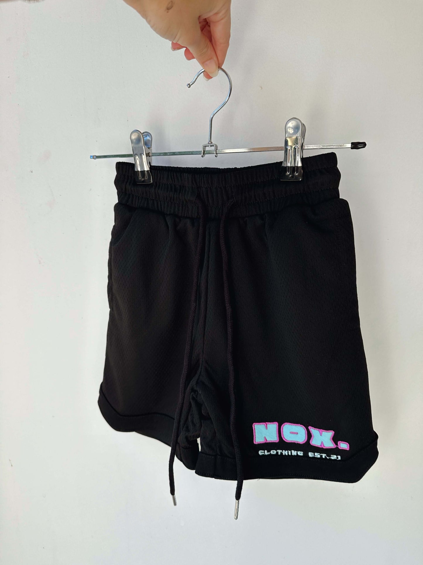 Black basketball shorts with elasticated waistband and side pockets, featuring a Tackle Twill signature logo, hanging on a clothes hanger.