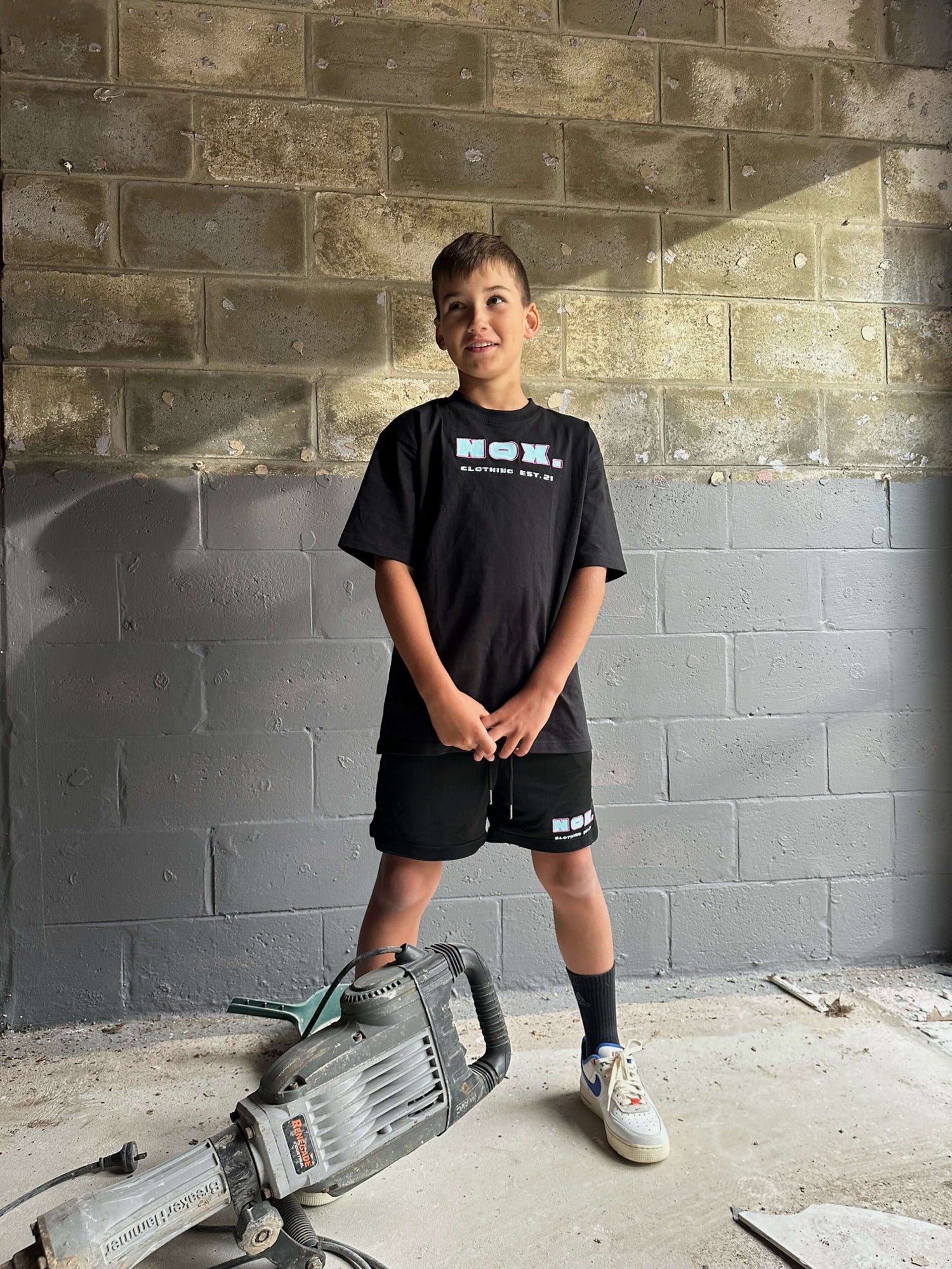 Young boy wearing comfy black basketball shorts with side pockets, elasticated waistband, and drawstring, standing in front of a concrete wall.